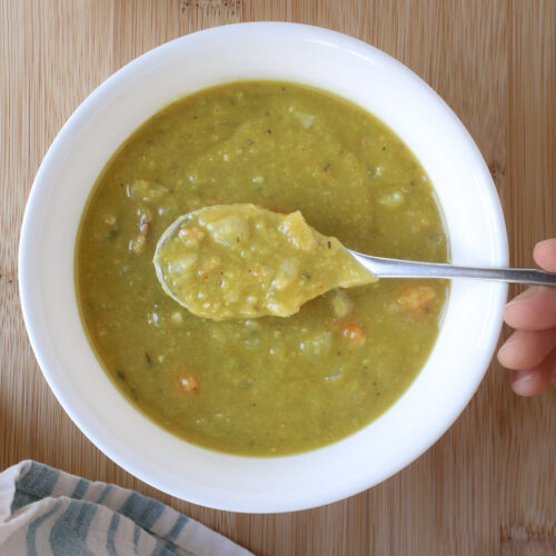 spoonful of split pea soup over bowl, with blue striped cloth nearby.