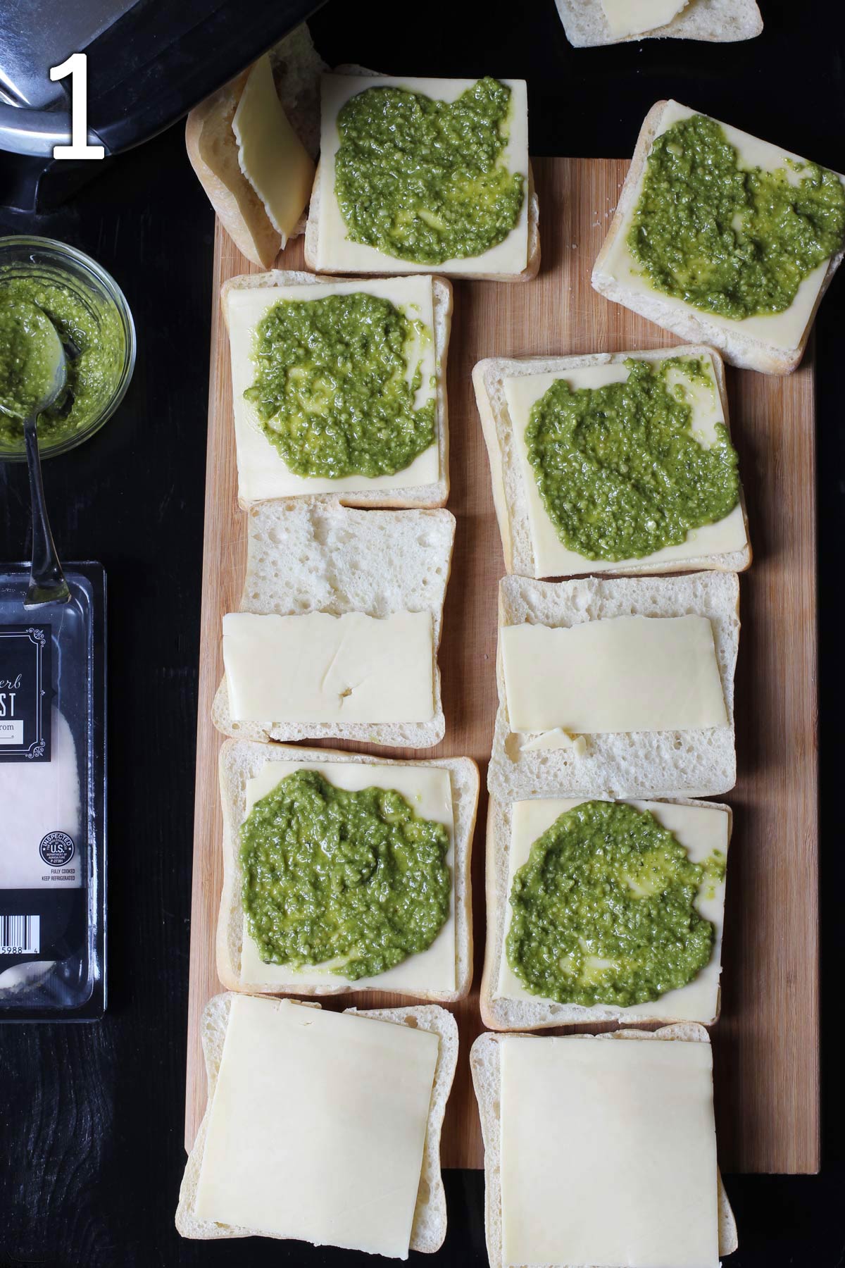 ciabatta rolls open with pesto and cheese on wooden board.