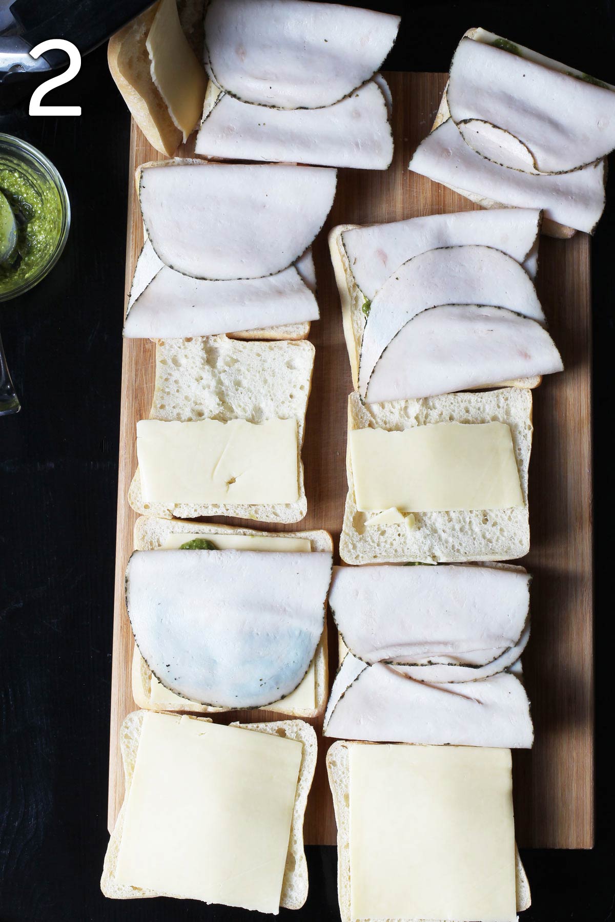 ciabatta rolls open on wood board with turkey, cheese, and pesto.