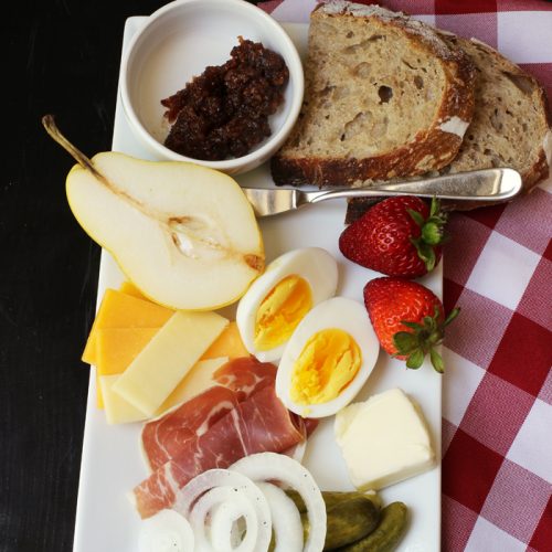 plate of meats, cheeses, egg, fruit, and pickle