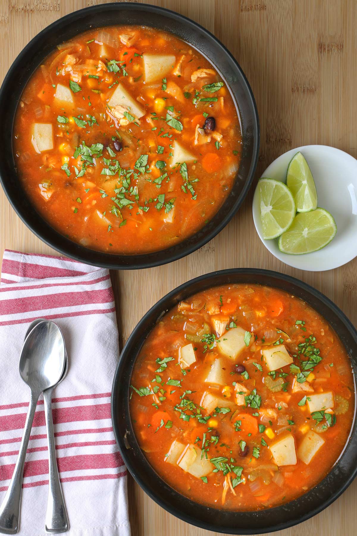 two bowls of chicken taco soup on table with lime wedges and spoons.