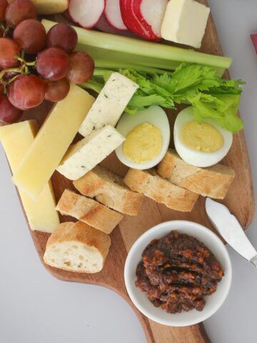 close up of ploughman's lunch on a wooden board with a red checked cloth.