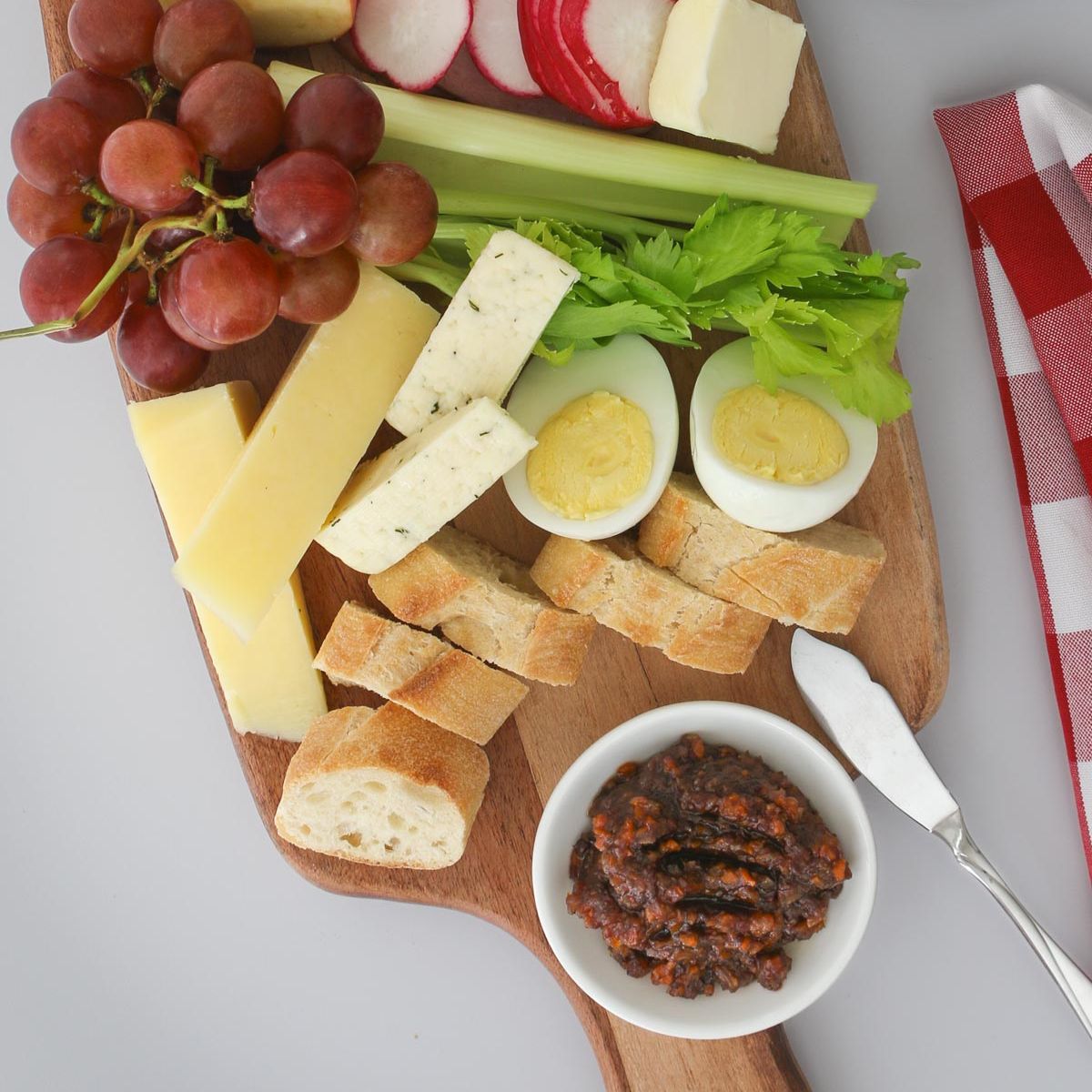 close up of ploughman's lunch on a wooden board with a red checked cloth.