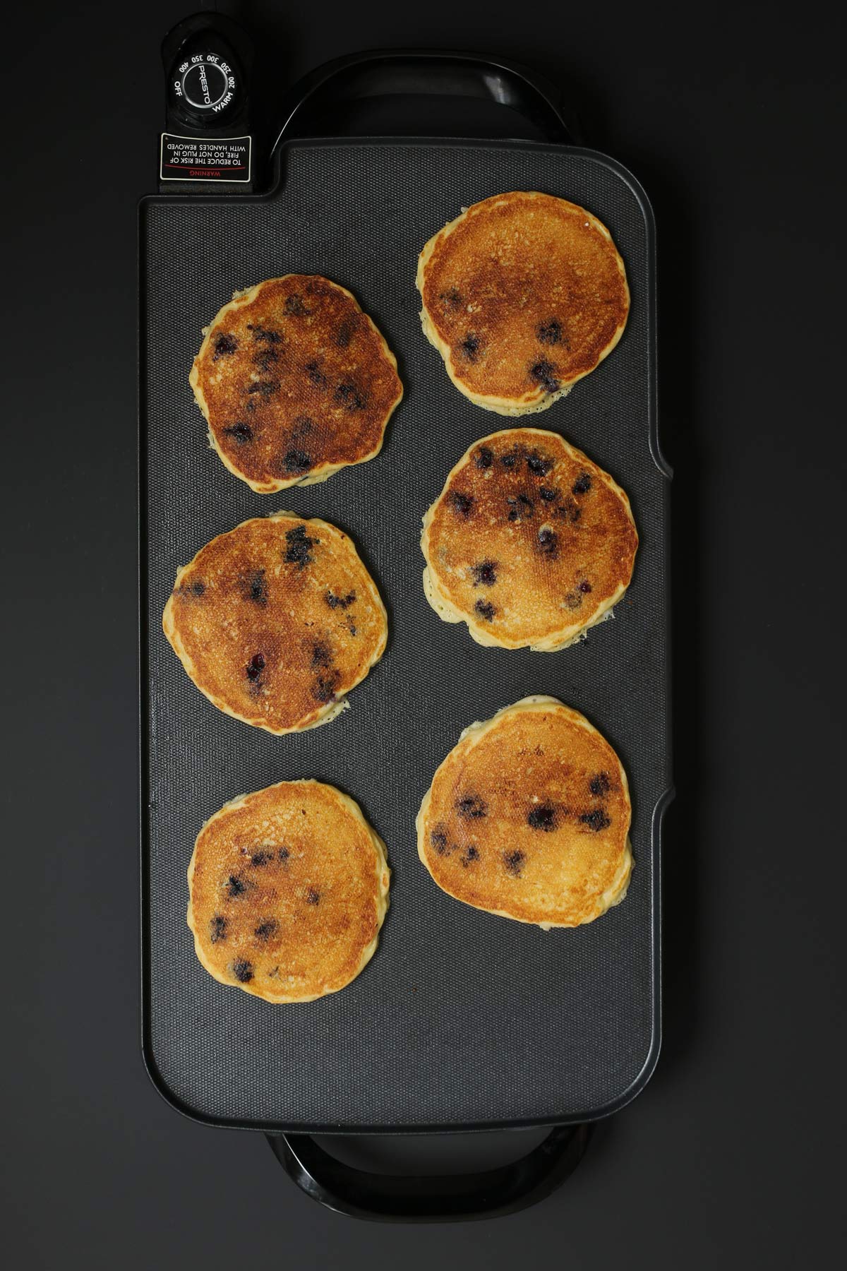 six cooked blueberry pancakes on the electric griddle.