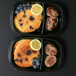 blueberry lemon pancakes in meal prep boxes with sausage patties in the smaller compartment.