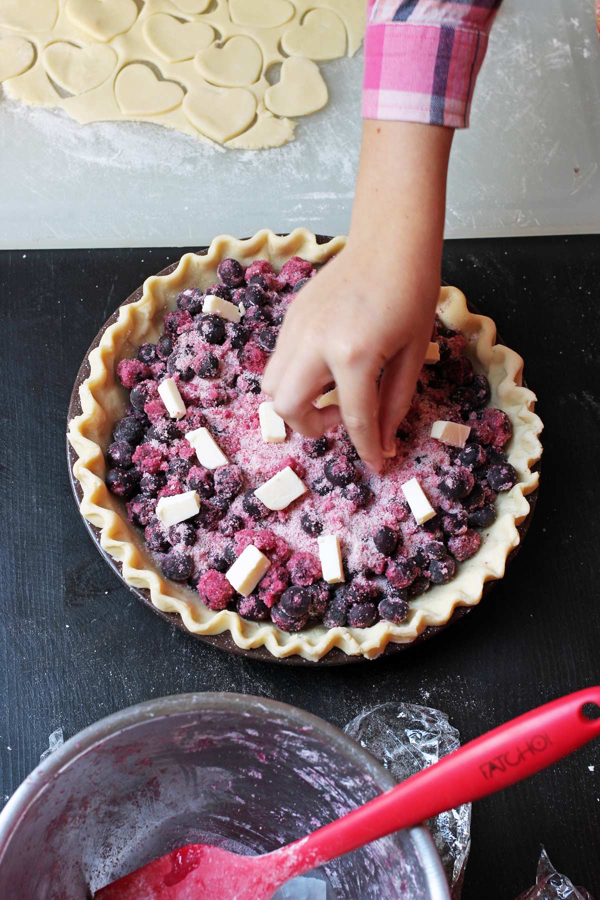 girl adding butter cubes to blueberry pie filling