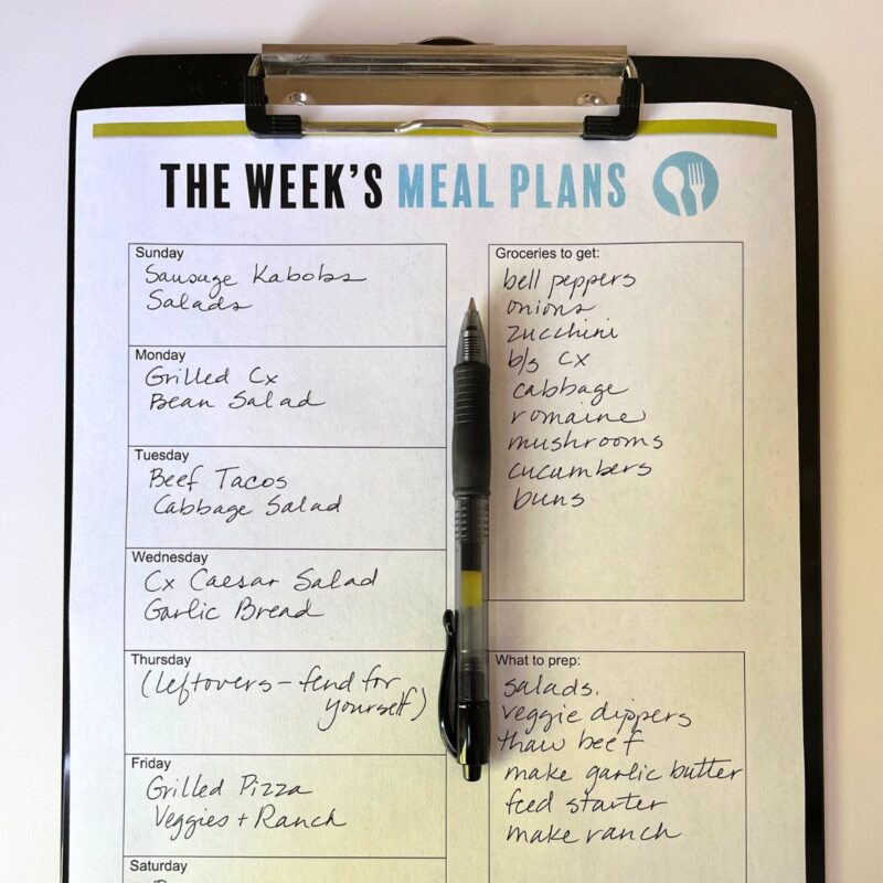 pen sitting on a printable meal plan on a black clipboard on a white table.