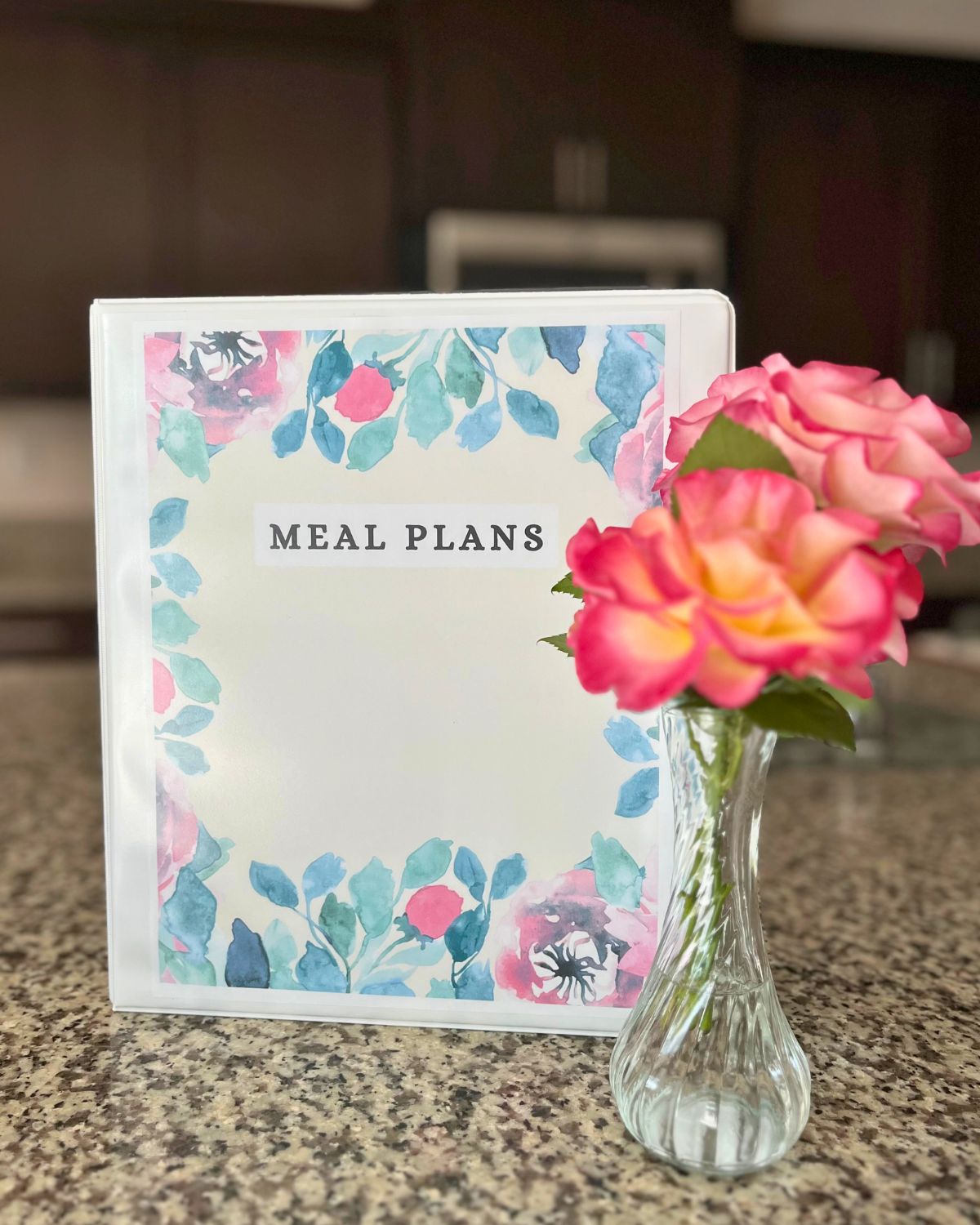 meal plans notebook on counter next to vase of flowers.