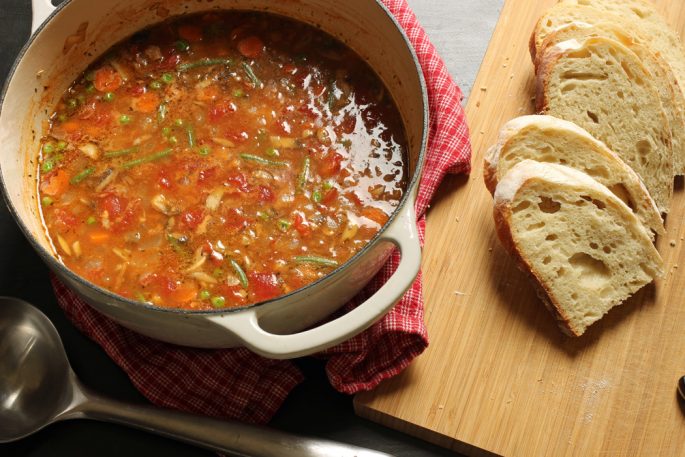 pot of tomato based soup with slices of bread on cutting board