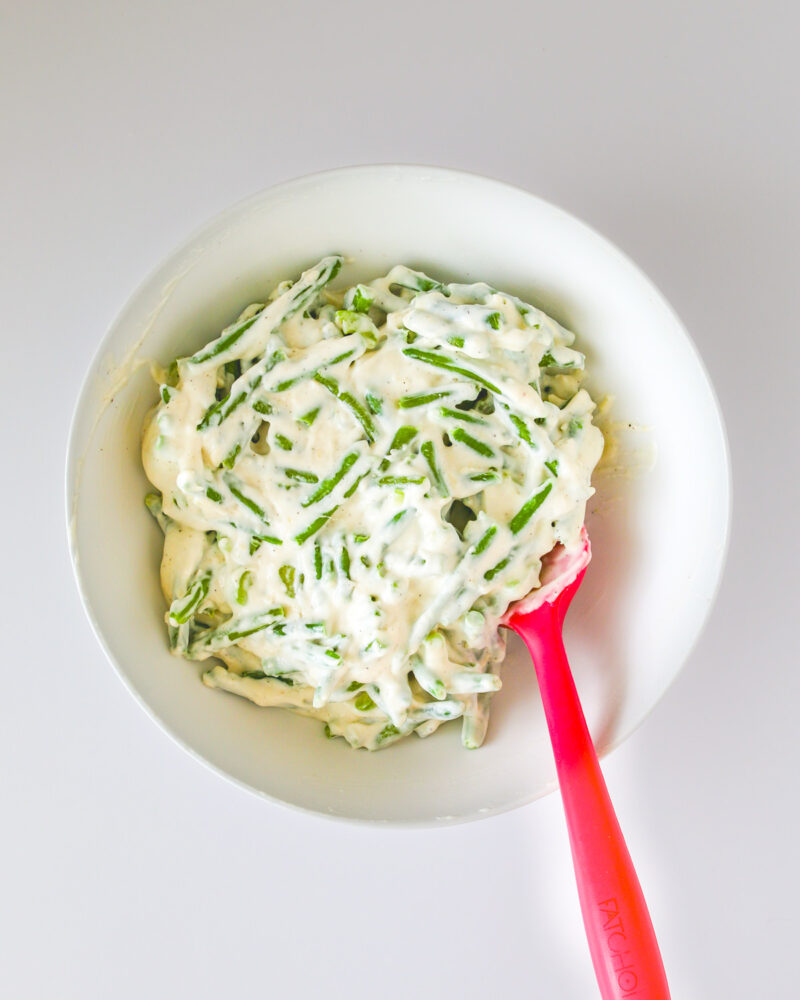 green bean mixture with sauce in bowl with red spatula.
