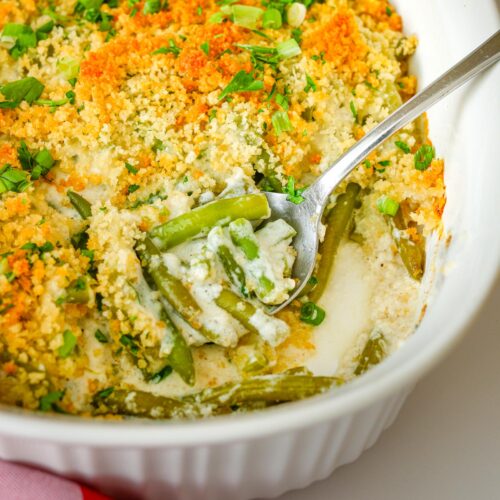 close up of green bean casserole with spoon inserted in the baking dish.