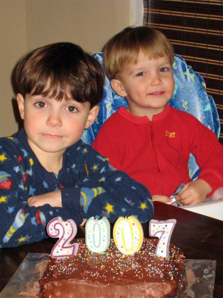 two boys in sleeper jammies at kitchen table with a cake with 2007 candles in it.