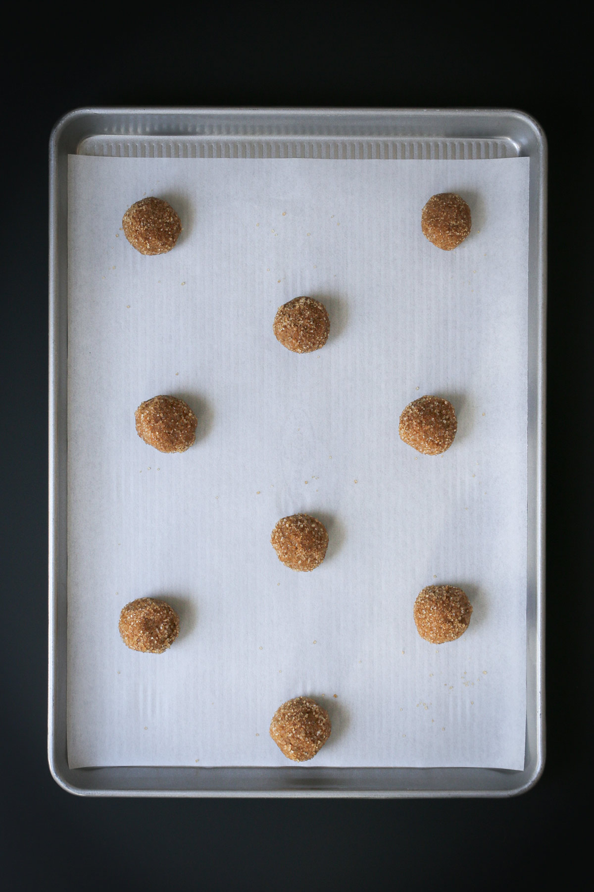 nine dough balls spread out on parchment on baking sheet.