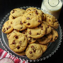 overhead view of chocolate chip cookies on glass platter with carafe of milk.