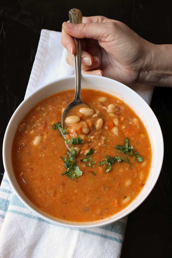 woman's hand holding spoonful of bean soup next to bowl