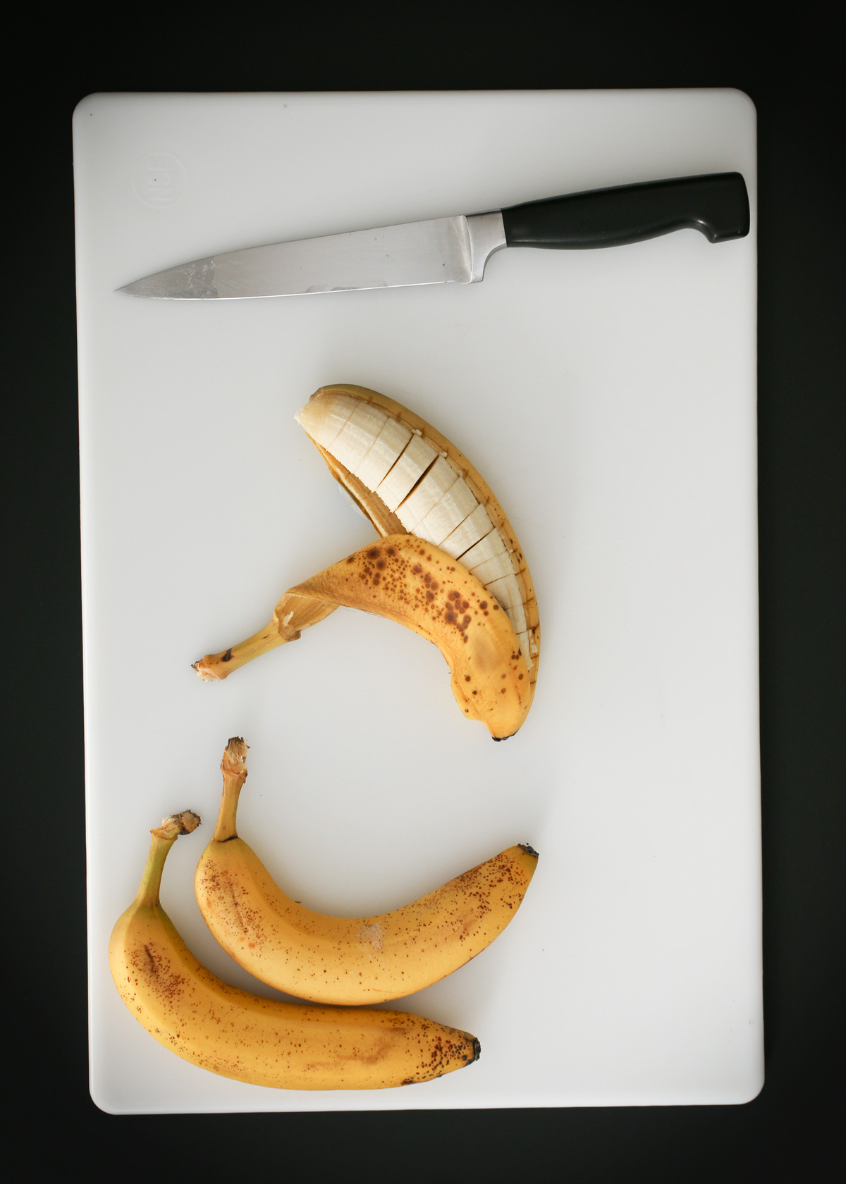 slicing bananas on cutting board with a chef's knife.