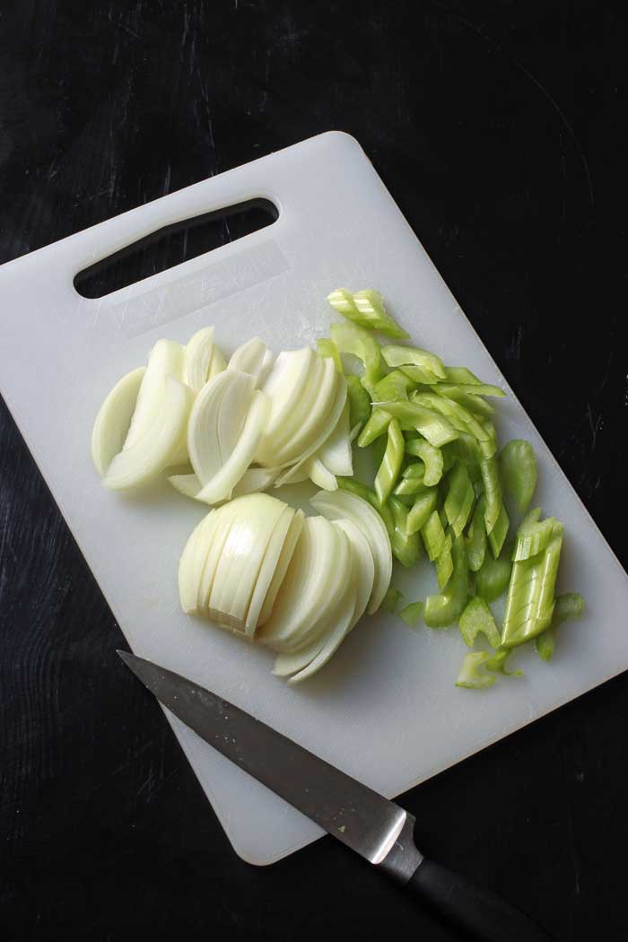 sliced onions and celery on cutting board with knife