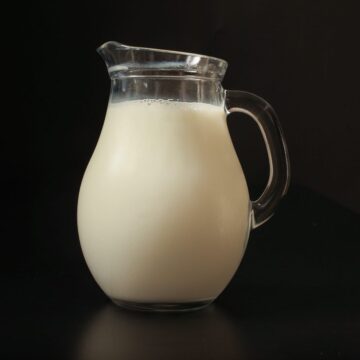 small glass pitcher of milk on black background.