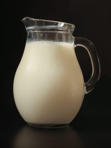 small glass pitcher of milk on black background.