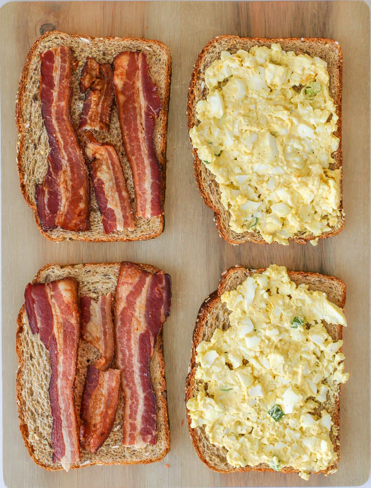 two sandwiches laid open, bacon on one side, egg salad on the other.