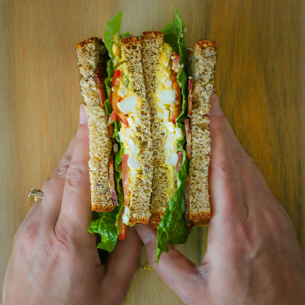 two hands holding two halves of a blt egg sandwich together with the cut sides up.