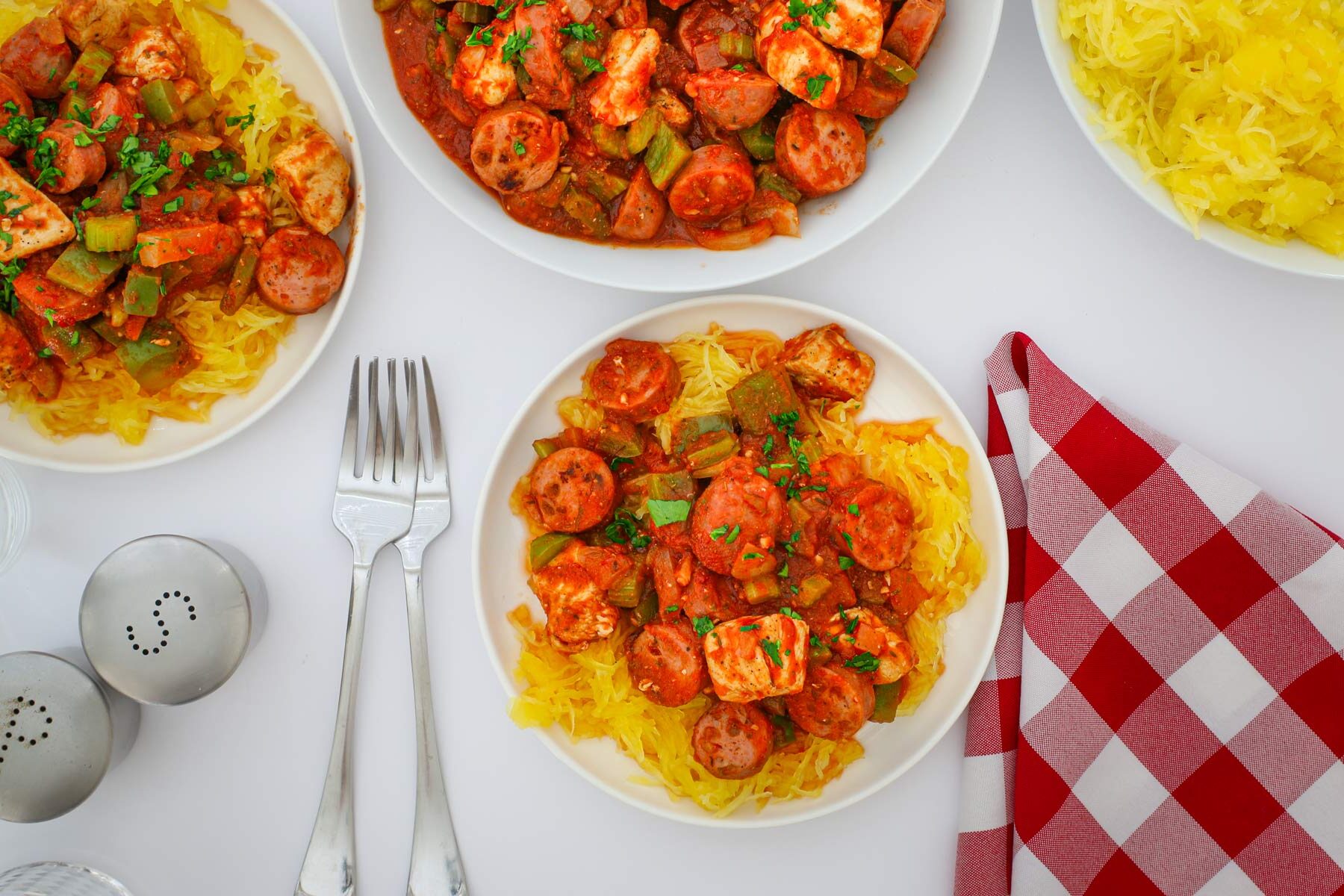 array of plates with spaghetti squash jambalaya on dinner table with napkins and cutlery.