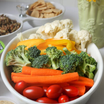 white platter of veggies on table with other snacks and vase of flowers.