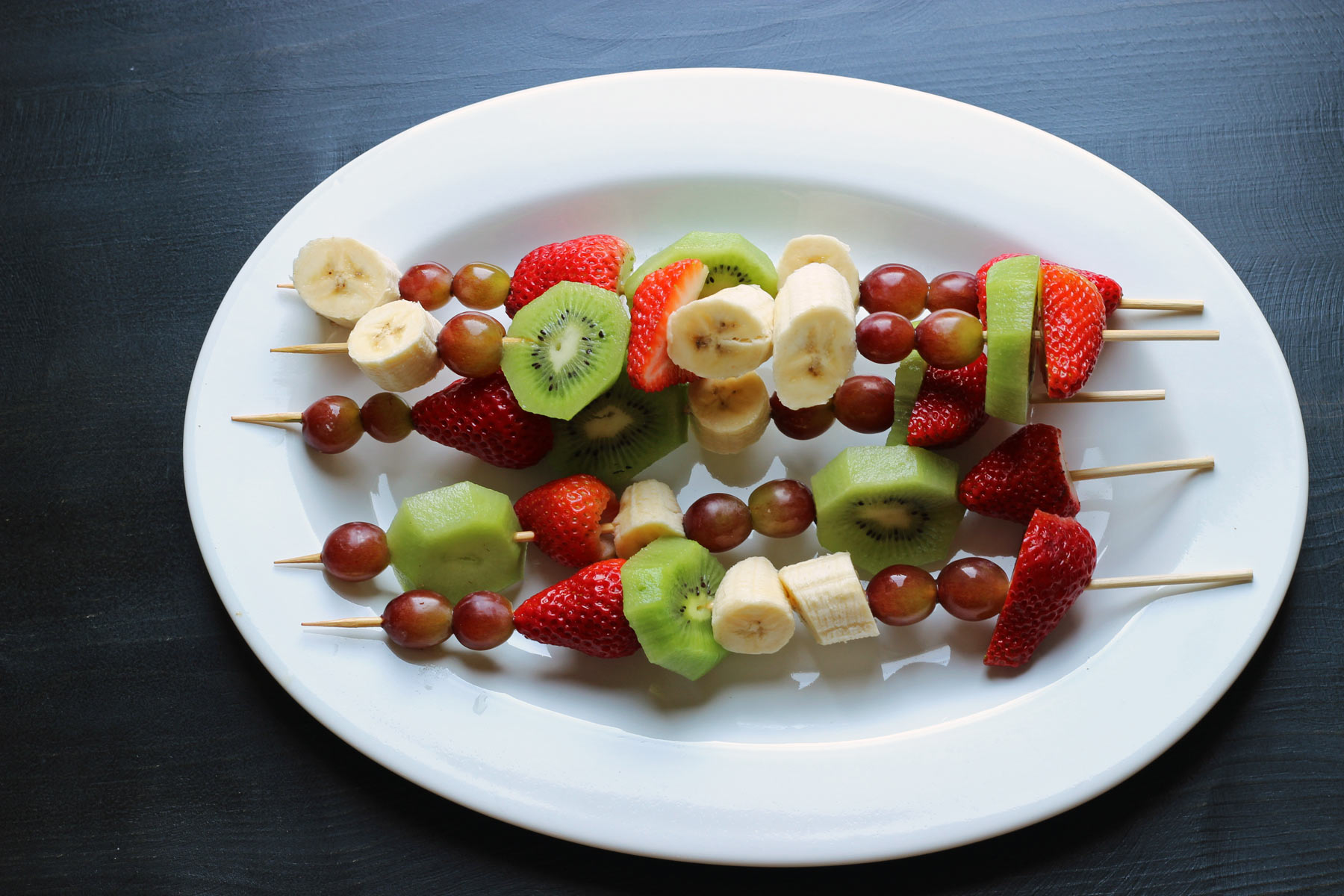 white oval platter with fruit skewers.