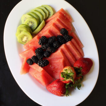 fruit tray with kiwi, melon, and berries on white oval platter.