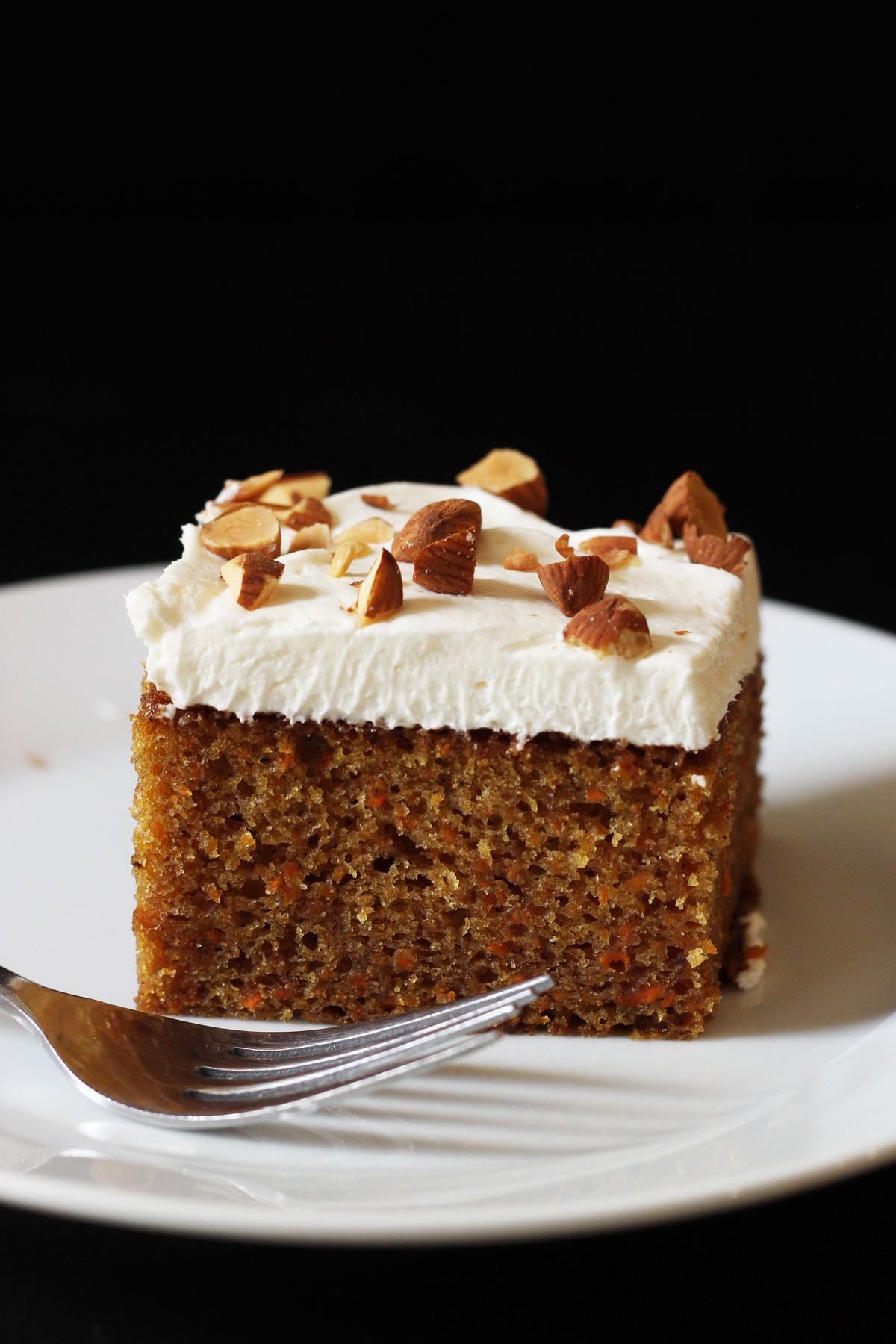 square of carrot cake on white plate with fork.