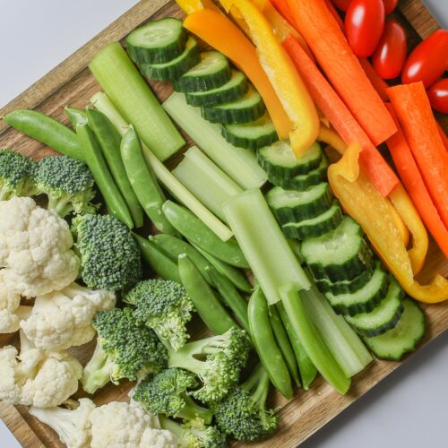 veggie tray made on wooden board on a diagonal on a white counter.