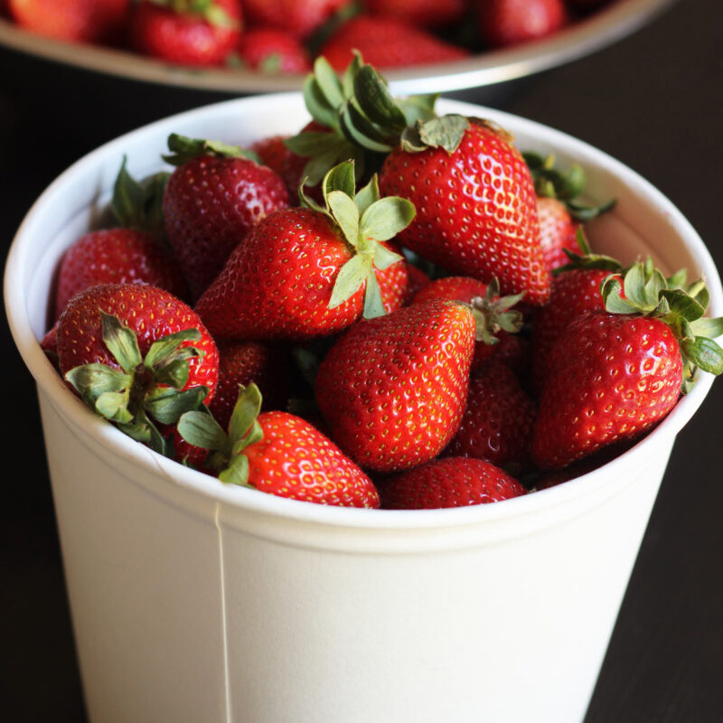 strawberries in white bucket on table with bowl of berries.