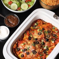 enchiladas in a casserole crockpot with side dishes on table