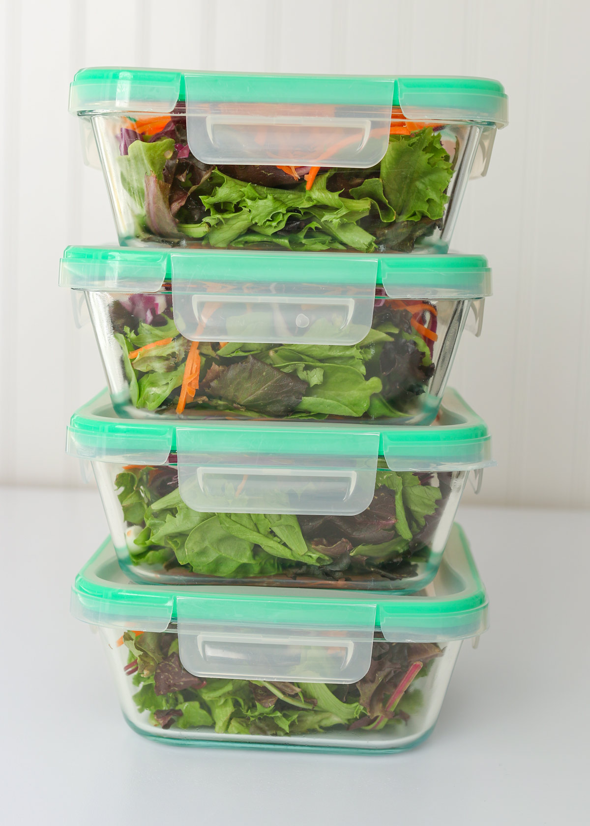stack of meal prep salads in glass boxes with green trimmed lids.