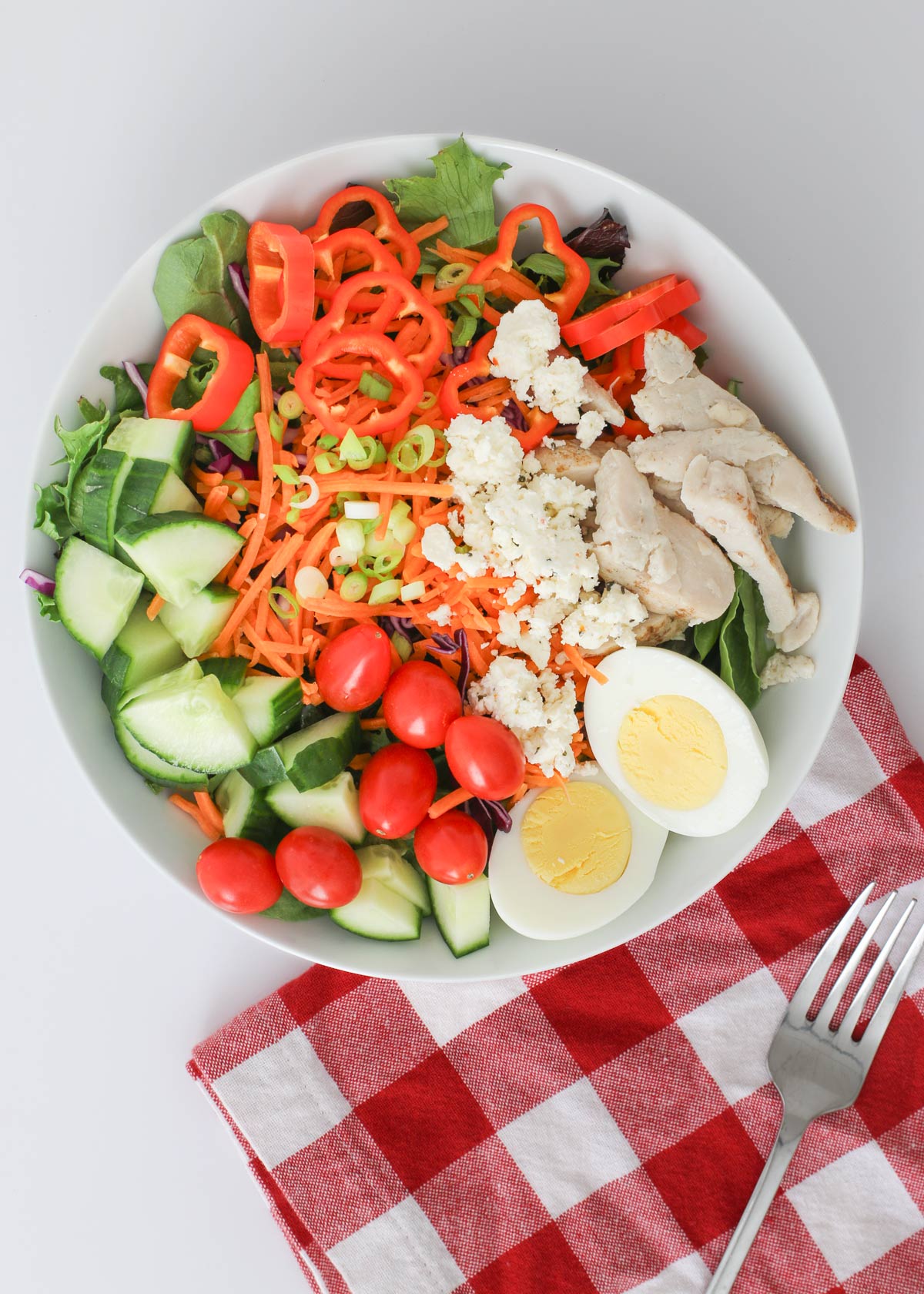 meal prep salad topped with egg, chicken, tomatoes, and cheese.