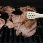 tongs holding up piece of grilled sirloin tip above the grill.
