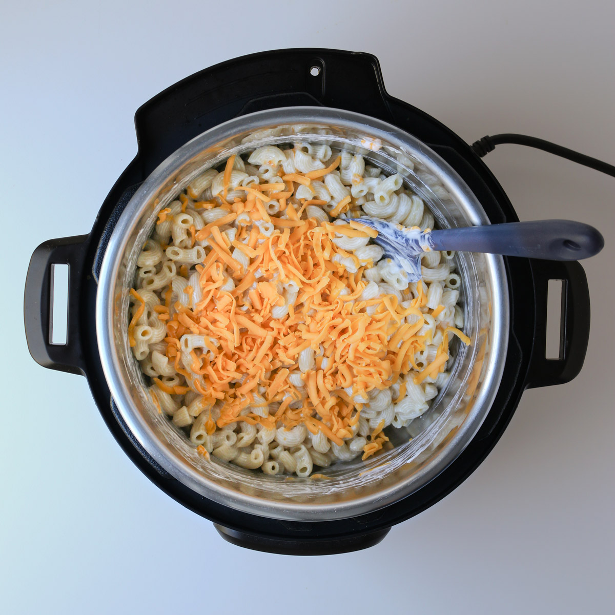 adding cheese to mac and cheese in pot.