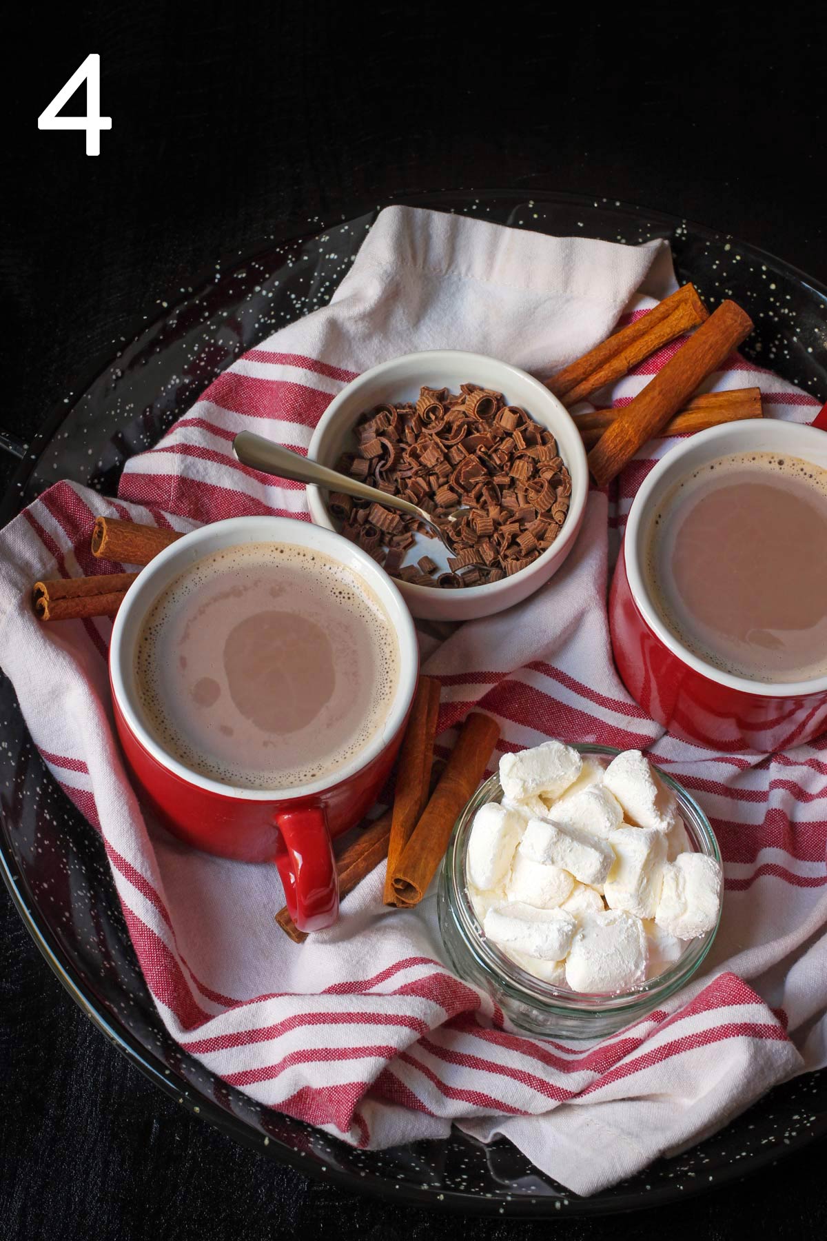 hot cocoa poured into mugs with bowls of toppings nearby.