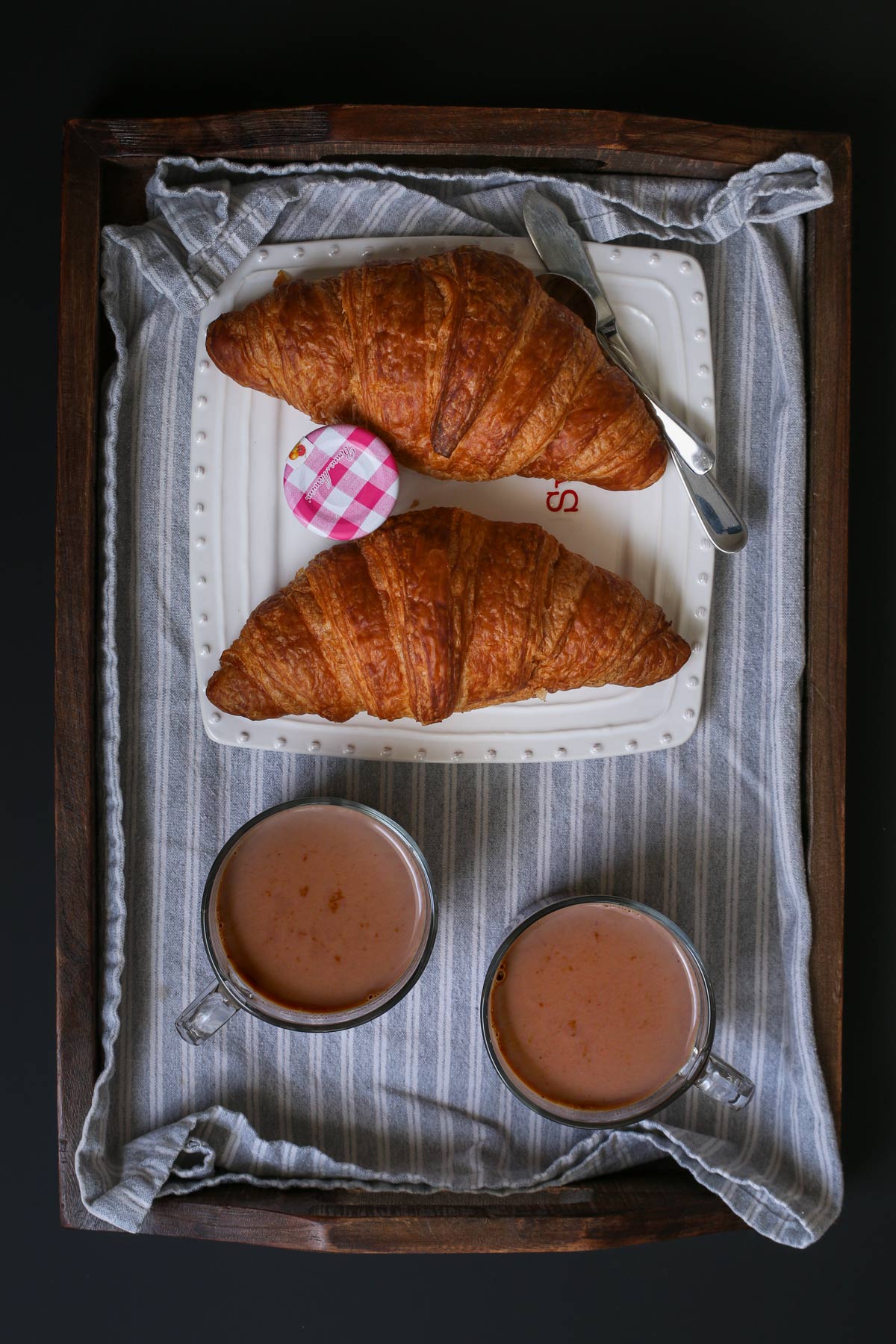 two mugs of hot cocoa with two croissants on a plate.