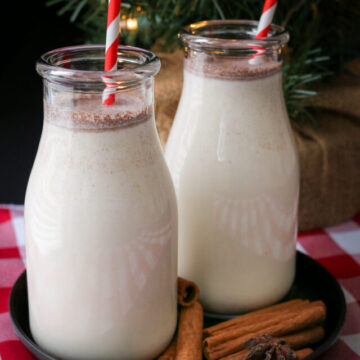 two milk bottles of eggless egg nog in front of a tree, with cinnamon sticks.