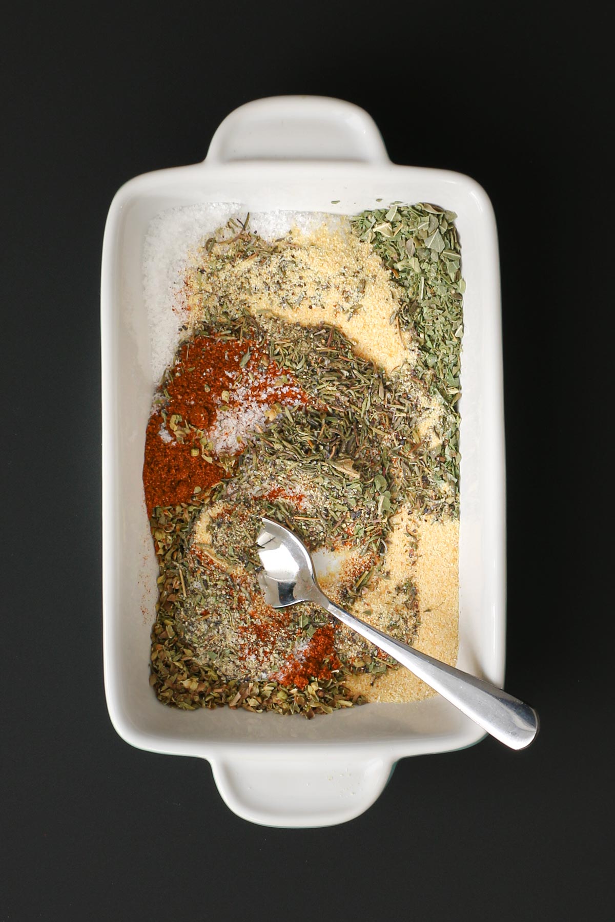 mixing the herbs and spices in white dish with a small spoon.