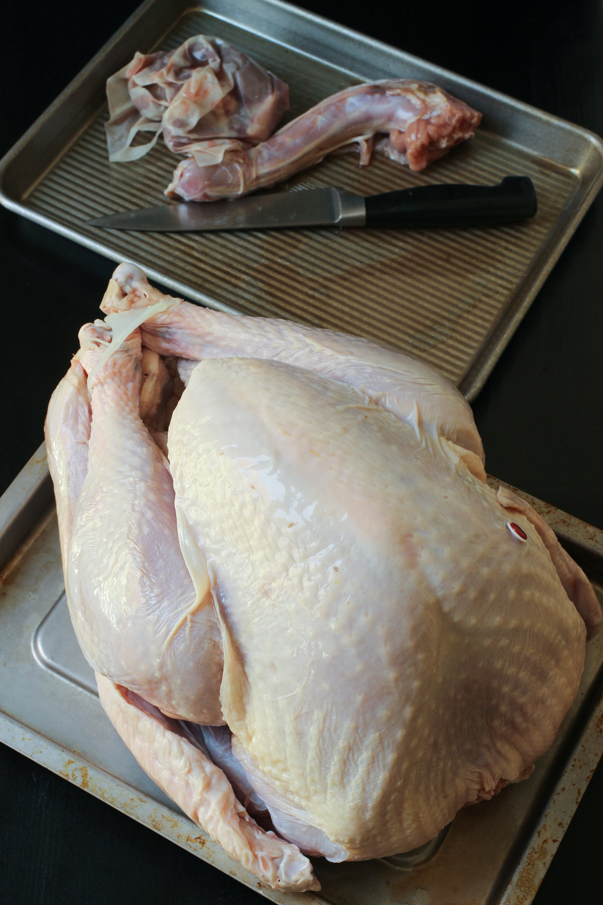 whole turkey removed from its wrapping on a tray with neck and giblets and a chef's knife on another tray nearby.