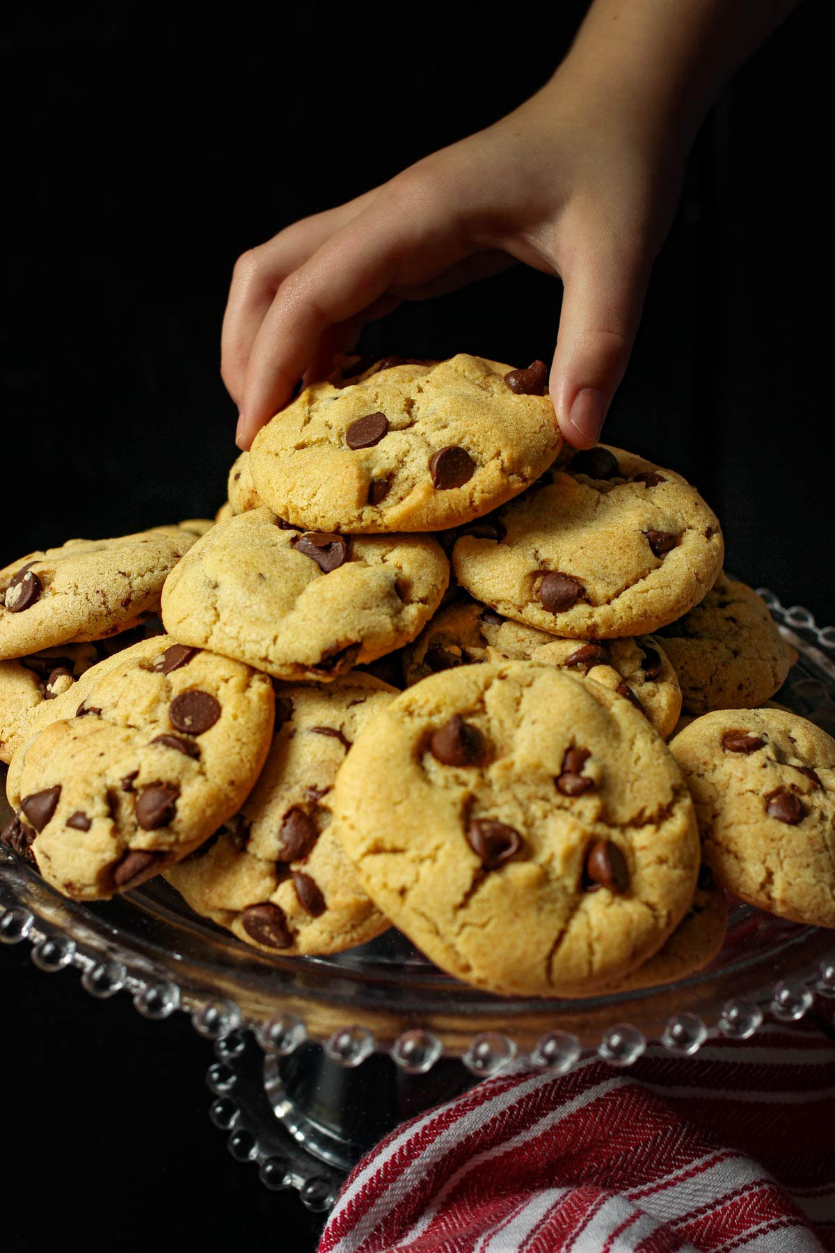 girl's hand reaching for a chocolate chip cookie from a stack on a platter.
