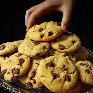 close up of chocolate chip cookies on a stack with a child's hand reaching for one.