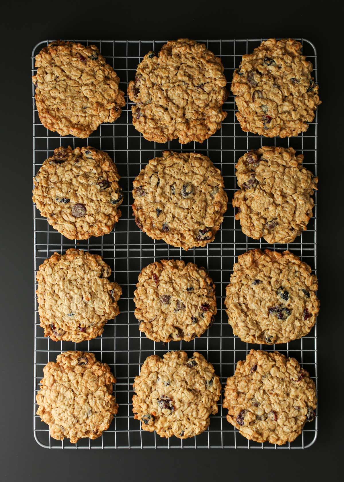 array of oatmeal craisin cookies on wire rack on black table.