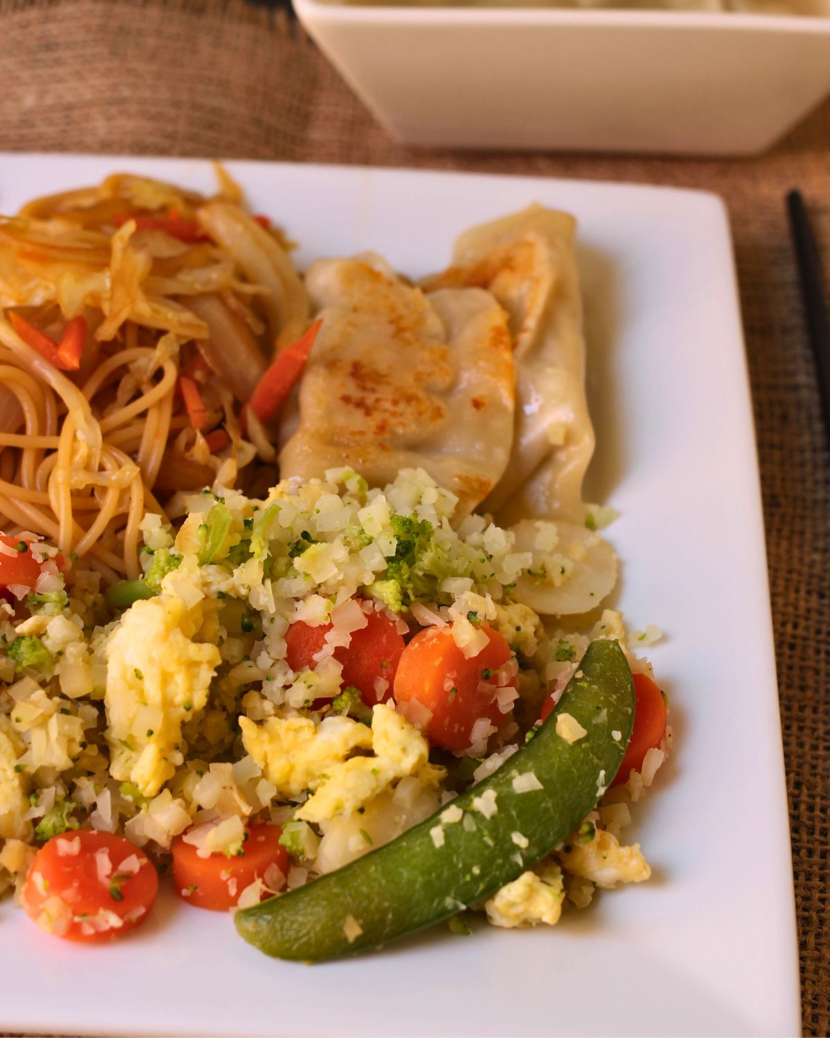 dinner plate with cauliflower stir fry, noodles, and potstickers.