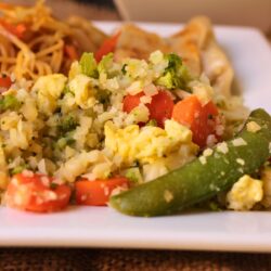 close crop of cauliflower stir fry on plate with noodles on side.