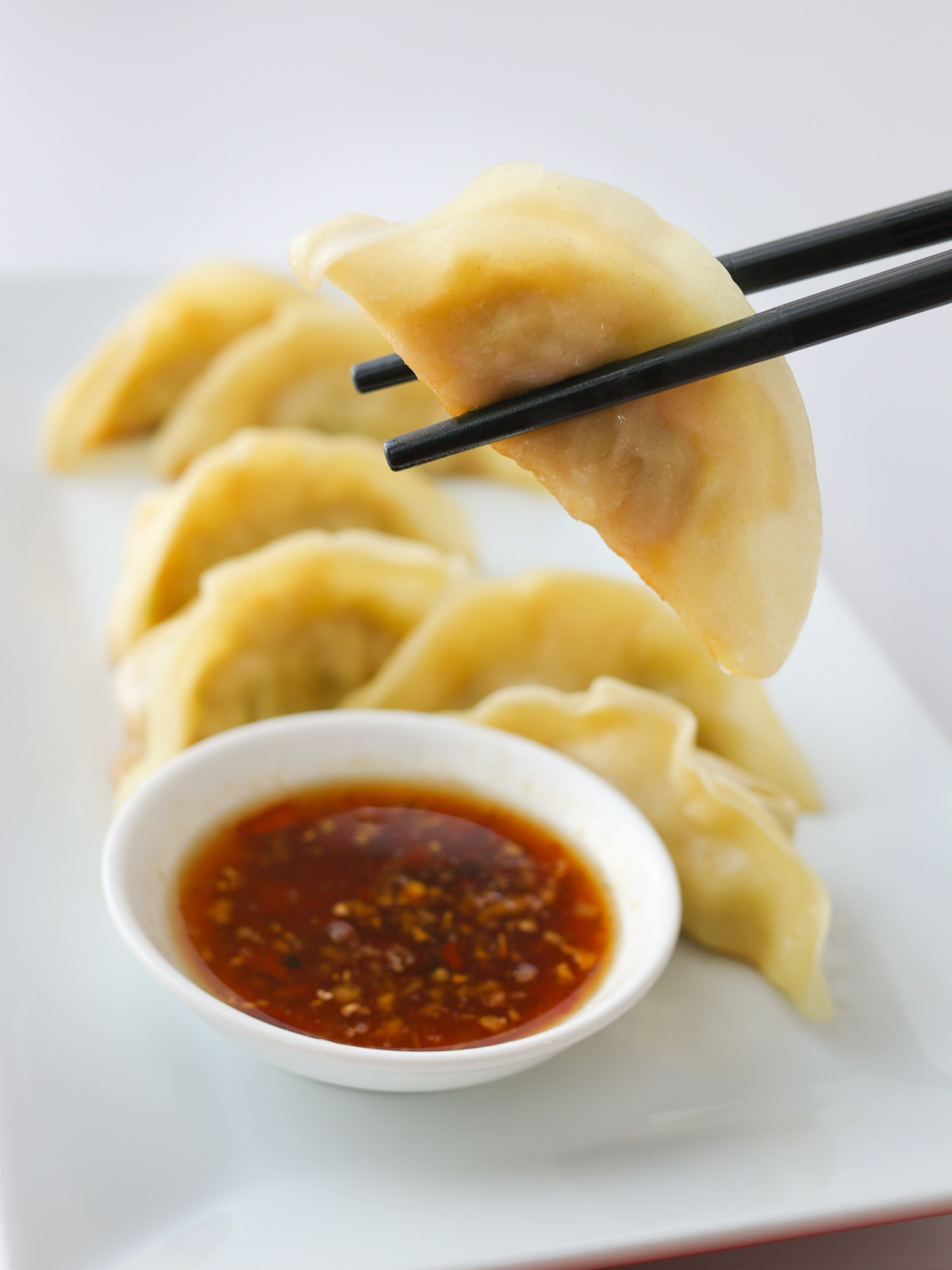 holding a potsticker in chopsticks above a platter of potstickers with dipping cup of sauce, 