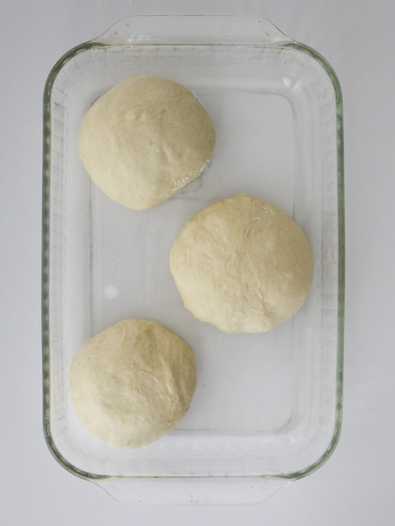 the dough balls resting in a glass dish.