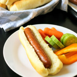 hot dog in homemade hot dog bun on plate with veggie dippers.